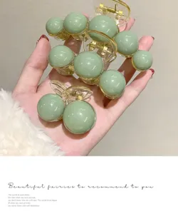 Detail view of sage green beaded hair claw clips with smooth round finish and clear base.
