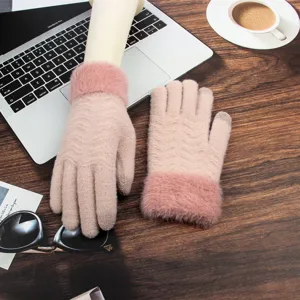 Close-up of pink knitted winter touchscreen gloves with furry cuffs on a wooden table.