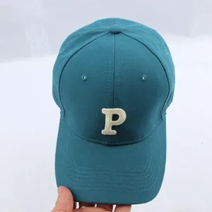 Baseball cap detail close-up showing white embroidered letter P on teal fabric surface.