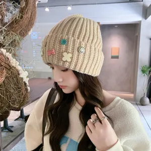 Beige knitted beanie hat with cute charms, thick warm winter headwear for women detail view.