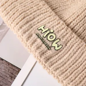 Gebreide muts detail close-up, beige winter warme zachte wollen muts met metalen letterbadge.