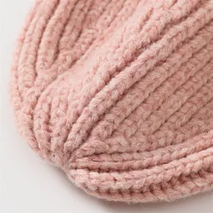 Close-up detail of soft pink knitted beanie hat showing thick ribbed texture and warm fabric.