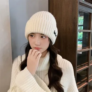 Close-up detail of women's ribbed knit beanie in solid cream white with side embroidery.