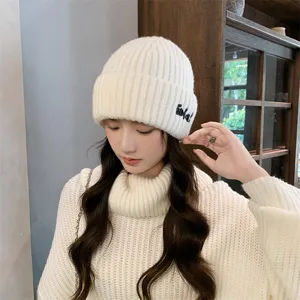 Close-up detail of a soft white ribbed knit beanie hat featuring chic side embroidery.
