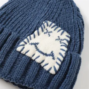 Nahaufnahme einer blauen Strickmütze mit weißem Flicken und niedlichem gesticktem Gesicht.