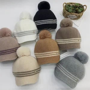 Detailed shot of multi-color knitted pom-pom beanies with striped design and metallic charm.