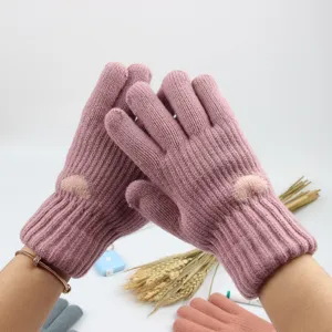Close-up detail of cozy pink knitted winter gloves featuring cute heart pattern and warm fleece.