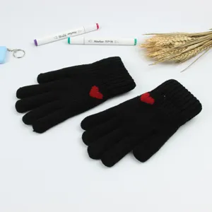 Close-up detail of black knit gloves featuring a cute red heart pattern for winter warmth.