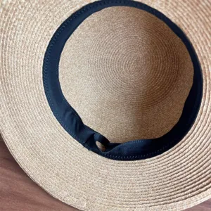 Close-up detail shot of the woven straw hat interior, showing neat black inner ribbon trim.
