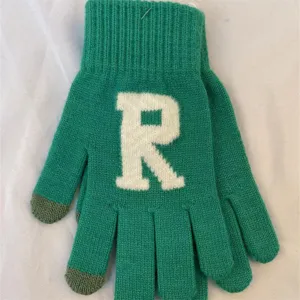 Détail de gants d'hiver tricotés verts tactiles avec un motif de lettre R blanche.
