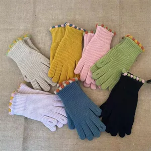 Close-up of colorful knitted winter gloves showing cute pom-pom trim and soft textured cuffs.