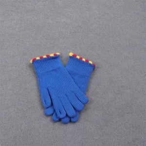 Close-up of winter warm knitted gloves with blue body and colorful pom-pom cuffs detail.