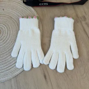 Detailed view of white knitted gloves featuring cute pink and green ruffled cuffs.