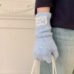 Light blue knitted fingerless gloves detail shot showing delicate lace embroidery patch.