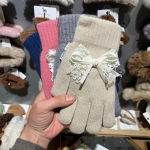 Detailansicht süßer Strick-Fünffingerhandschuhe mit weißer Spitzen-Schleife und Perle.