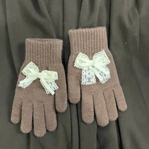 Detailansicht brauner Strickhandschuhe mit eleganten cremefarbenen Schleifen im Herbst.