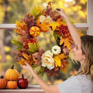 Detailed view of an autumn wreath with pumpkins and leaves held by a woman in a lifestyle setting