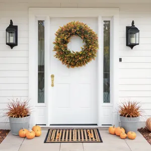 Large artificial autumn boxwood wreath hanging on a white front door with pumpkins