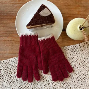 Close-up detail of red knitted winter gloves with white ribbed cuffs on a cozy wooden table.