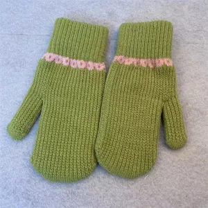 Close-up detail of winter warm knitted mittens, cozy green wool fabric with cute pink trim.