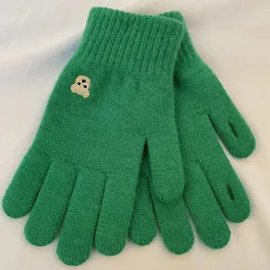 Close-up of green knit gloves with cute bear embroidery, soft and warm winter daily wear.