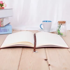 Detailed view of an open A5 leather notebook with brown ribbon bookmark on wooden table.
