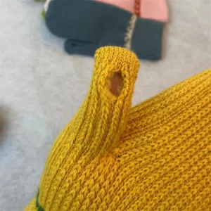 Close-up detail shot of yellow winter knitted touchscreen glove showing thumb opening feature.
