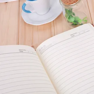Close-up view of open A5 leather notebook with lined pages, memo date fields and desk decor.