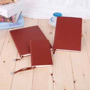 Detailed view of dark red leather office notebooks with ribbon bookmarks on wood table.