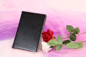 Detalle de cuaderno de cuero PU negro con logotipo en relieve, elegante arreglo de rosas.