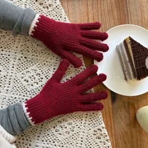 Close-up detail shot of winter warm knit gloves in deep red with white contrast cuffs on table.