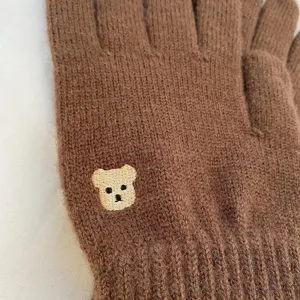 Detailed view of brown knit winter gloves featuring lovely embroidered bear detail.