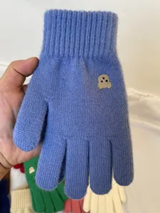 Close-up detail of winter knitted blue gloves featuring a cute embroidered bear pattern.