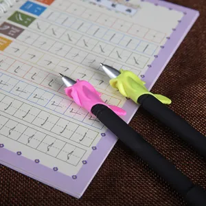 Detail shot of silicone pen grips in pink and green on pinyin practice copybook for student writing.