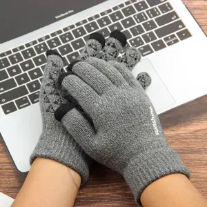 Close-up of grey knit touchscreen gloves featuring anti-slip grips on wooden desk laptop.