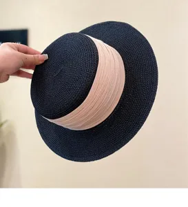 Black flat-top straw hat detail shot featuring wide beige ribbon and fine woven texture.