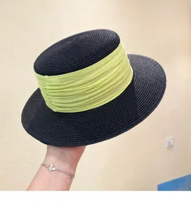 Detailed view of the black straw hat with vibrant green ribbon band, fine woven texture closeup.