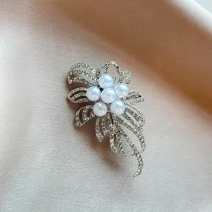 Close-up view of elegant floral brooch with sparkling rhinestones and white faux pearls detail.