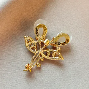 Detail shot of gold-toned leaf brooch back structure, showing pin clasp and white cabochons