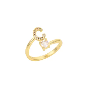 Détail d'une bague ouverte dorée avec une lettre C sertie de cristaux et une pierre