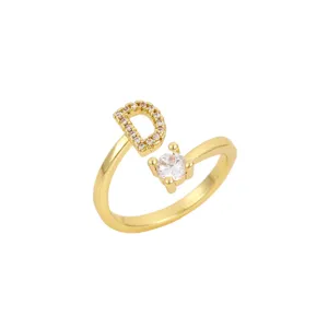 Détail d'une bague dorée ajustable avec la lettre D pavée et une pierre claire