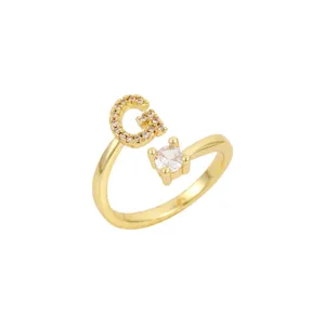 Vue macro détaillée d'une bague ouverte dorée avec un G en cristal et une pierre transparente