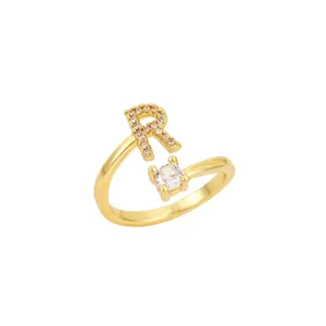 Détail d'une bague ouverte dorée ornée d'une lettre R pavée de zircons étincelants.