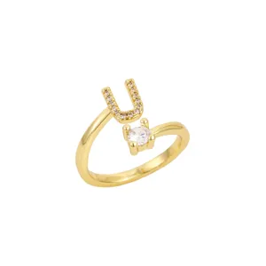 Détail d'une bague dorée ajustable avec une lettre U sertie et une pierre brillante