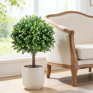 Weelderige kunstmatige Aglaia Odorata in witte pot naast een beige fauteuil in huis
