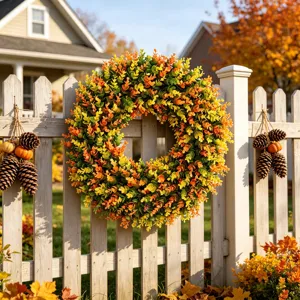 Artificial fall wreath with orange and yellow leaves hanging on white wooden fence