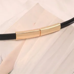 Gros plan d'une fine ceinture en cuir verni noir avec un fermoir en métal doré élégant.