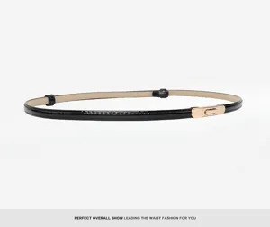 Close-up detail of the black patent leather thin belt with elegant gold metal buckle closure.