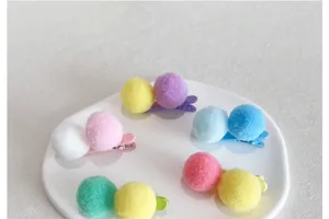 Gros plan de jolies pinces à cheveux à pompons en peluche colorés sur assiette.