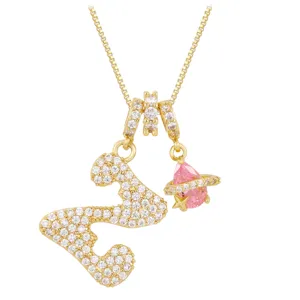 Macro detail of gold necklace featuring iced-out letter S and pink planet charm with star
